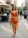 Model wearing orange floral chiffon halter crop top and layered mini skirt walking on city street